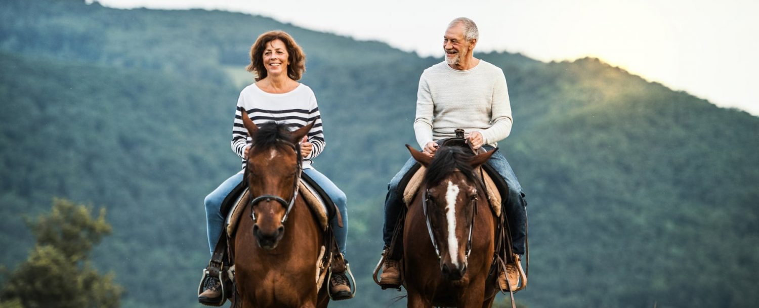 Older couple riding horses through the mountains.