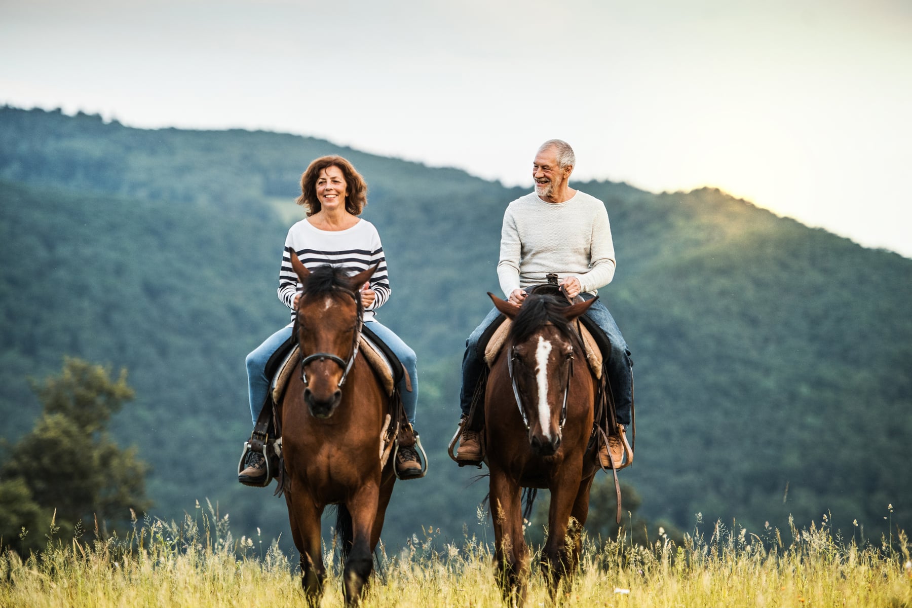 Older couple riding horses through the mountains.