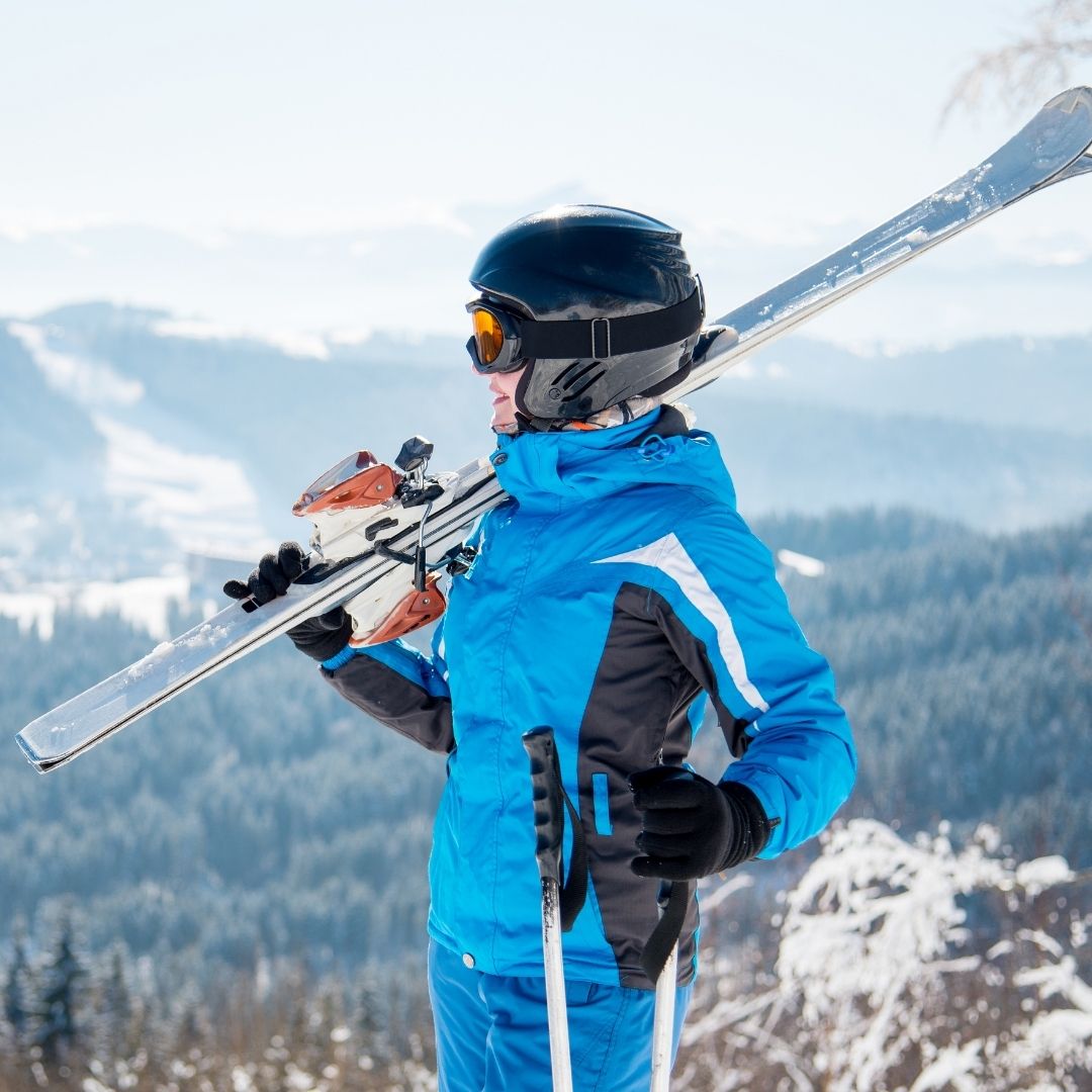 Woman standing on a mountain at a ski resort holding skis.