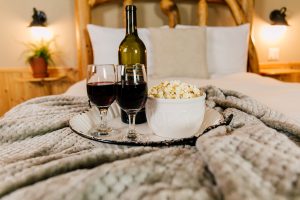 Tray with wine bottle, wine glasses and a bowl of popcorn sitting on bed
